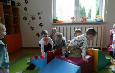 Sala zabaw-na podłodze leżą duże kolorowe piankowe klocki a na nich siedzą dzieci. 