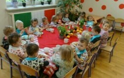 Zdjęcie przedstawia grypę dzieci w kolorowych ubrankach siedzących przy stole.